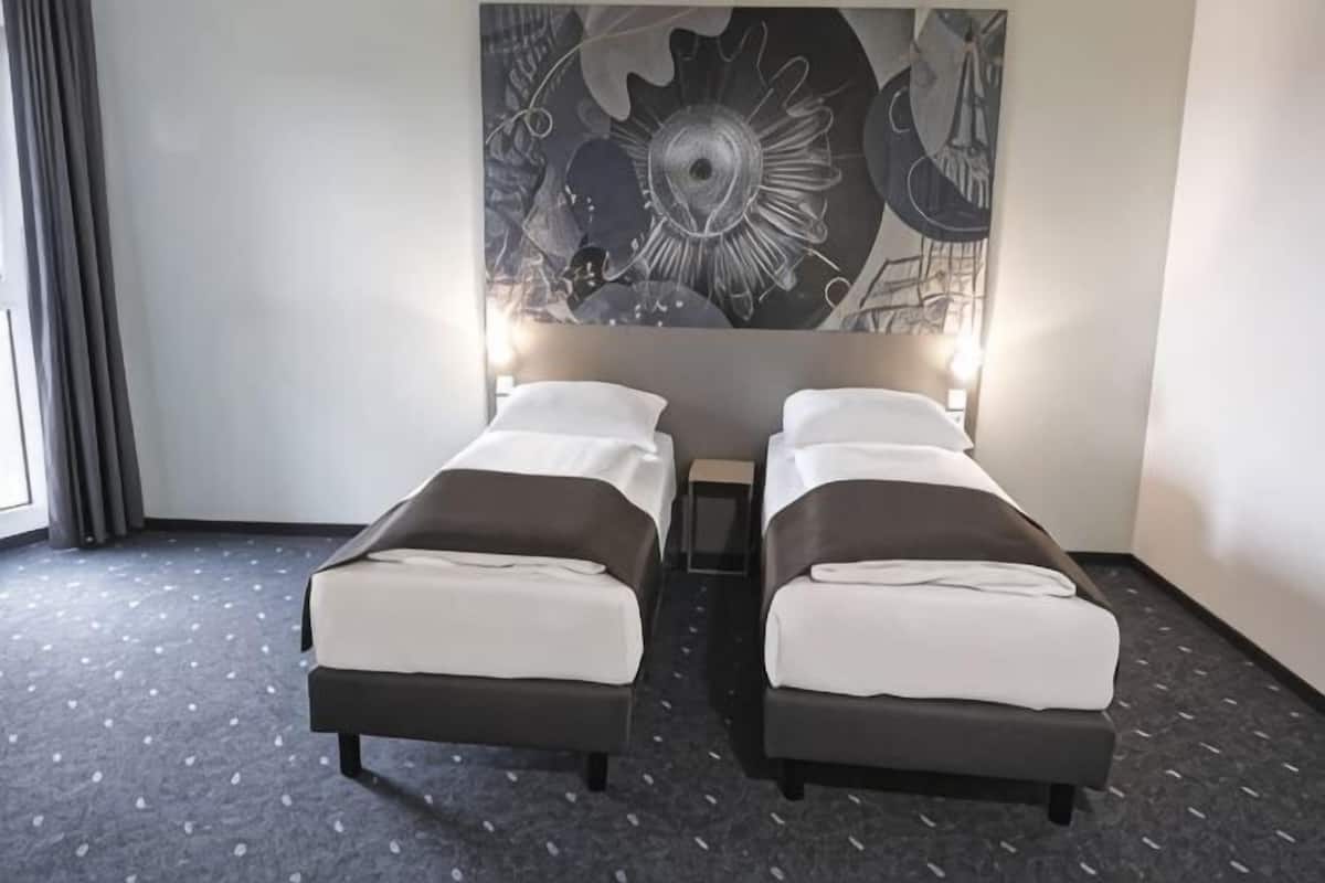 Habitación de hotel con dos camas individuales, una gran obra de arte abstracta en la pared y suelo alfombrado.