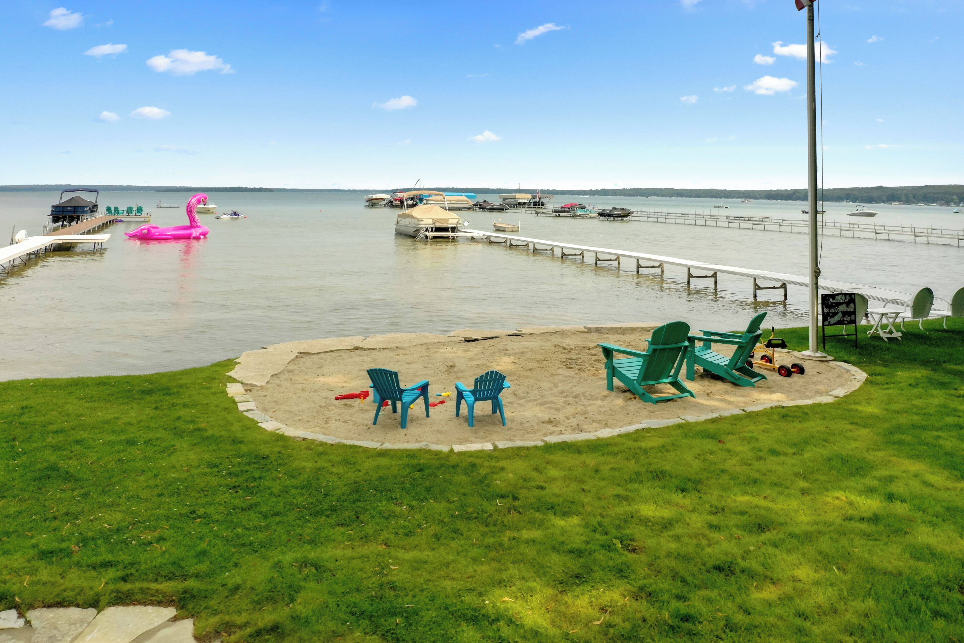 Une terrasse au bord du lac avec un espace sablonneux, des chaises vertes et un flamant rose gonflable.