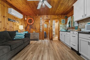 Cozy cabin-style accommodation with a comfortable sofa, kitchen area, and door to a bathroom.