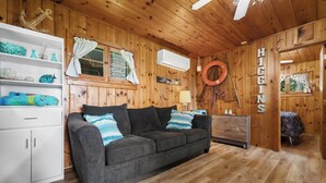 L’intérieur d’un chalet accueillant, avec un plafond en bois, un canapé gris agrémenté de coussins à motifs, une armoire blanche et un lit recouvert d’une courtepointe à motifs.