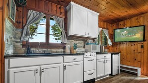 Une cuisine avec des meubles blancs, une cuisinière et un téléviseur fixé au mur.