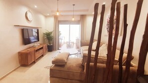 A living room with a flat-screen TV, wooden entertainment unit, beige sofa, and a dining area with a table and chairs.