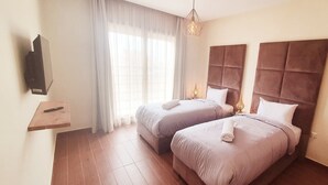 A hotel room with two beds, a TV, a small table, and a window with curtains.
