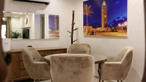A room with a round table and two chairs, a wooden cabinet, a mirror, and a painting of a tower at night.