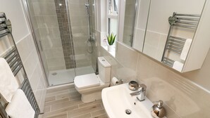 A modern bathroom with a glass-enclosed shower, a white toilet, a sink with a mirror, and a towel rack. - 8 Waterside Wood (Windermere)