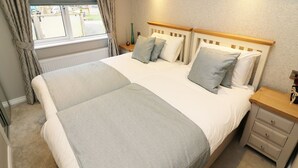 A neatly arranged bedroom with a large bed, bedside tables, and a window with curtains. - 8 Waterside Wood (Windermere)
