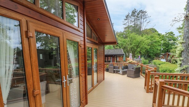 A wooden deck with glass doors leading to a patio area with outdoor furniture. - 8 Waterside Wood (Windermere)