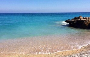 Une plage à l’eau turquoise et limpide, avec un rivage de galets et un promontoire rocheux.