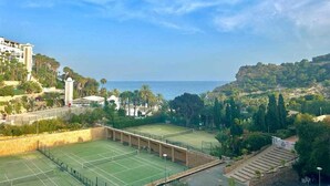 A tennis court with a clear view of the sea and surrounding greenery.