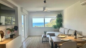 A modern living room with a dining area, large windows, and a view of the ocean.