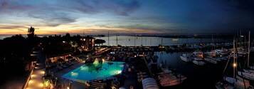 Un puerto deportivo al anochecer, con barcos amarrados, una piscina y vistas al agua.