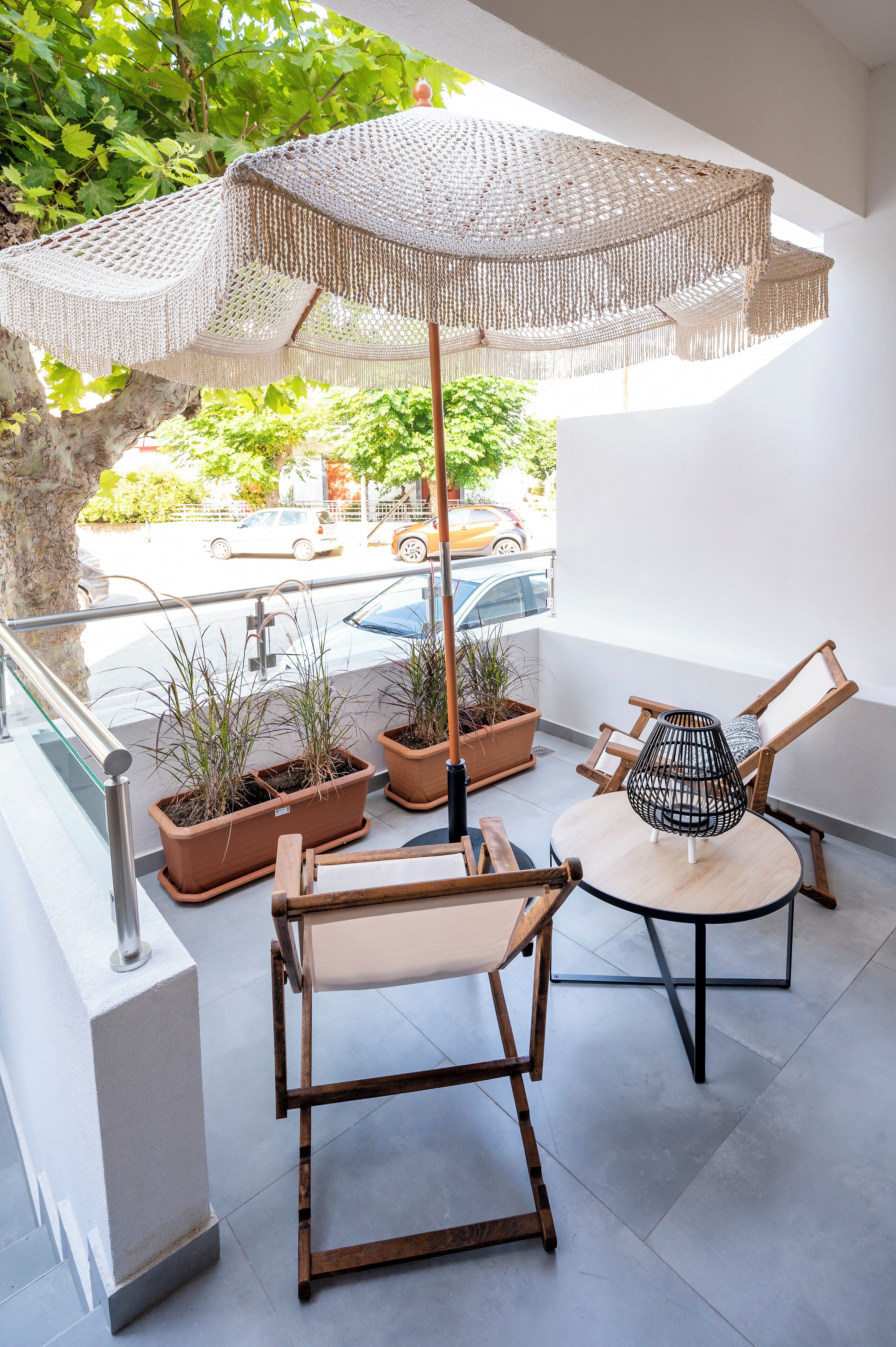 Un balcon agrémenté de meubles en osier, d’une table ronde et d’un grand parasol en fibres tressées. On y trouve des plantes en pot et une vue sur la rue.