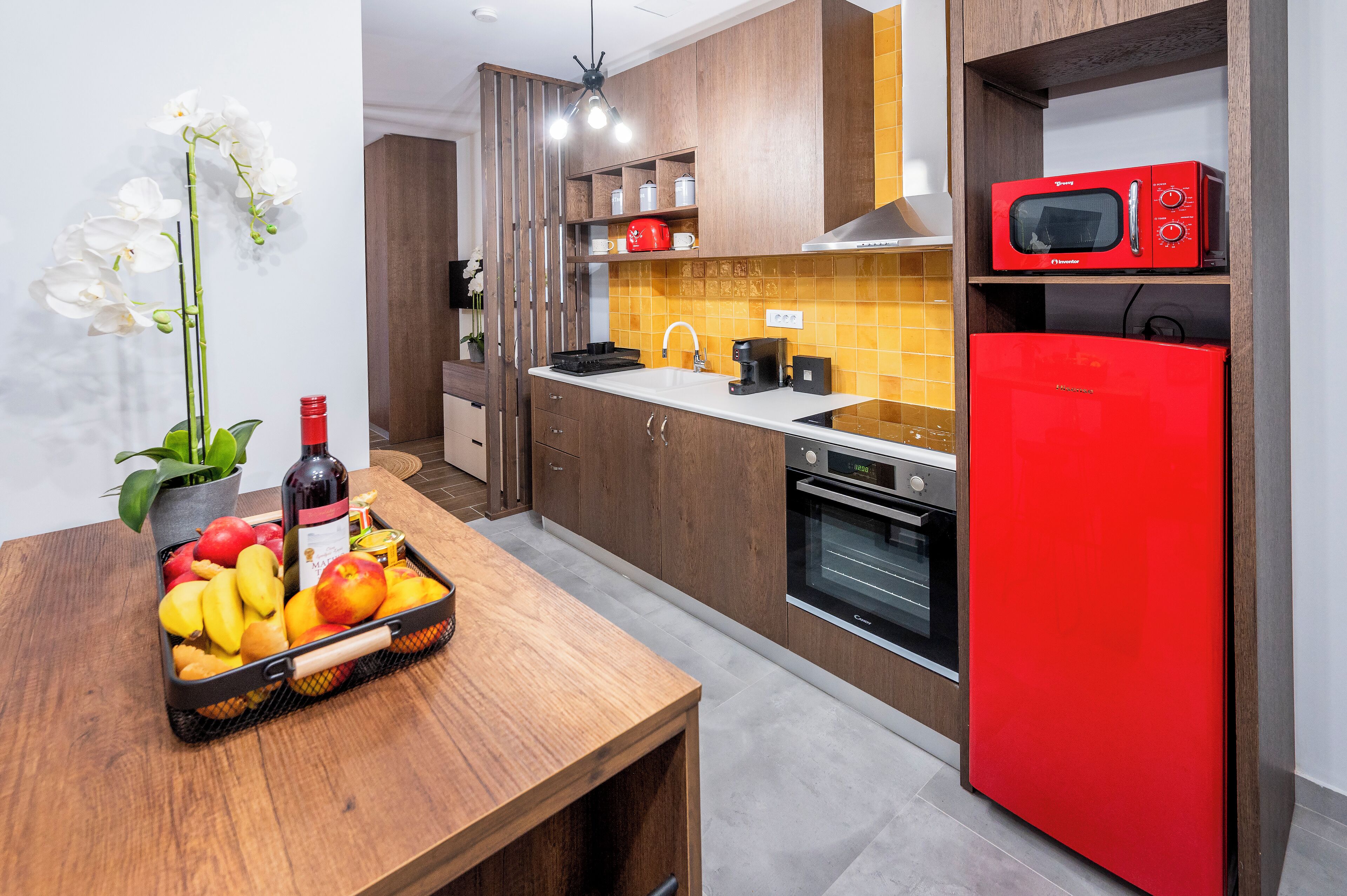 Cocina moderna con armarios de madera, un refrigerador rojo, un microondas y una cesta de frutas sobre la encimera.