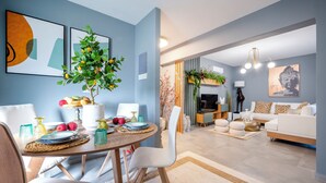 A modern living room with a dining area, featuring a round table, white chairs, and a potted plant.