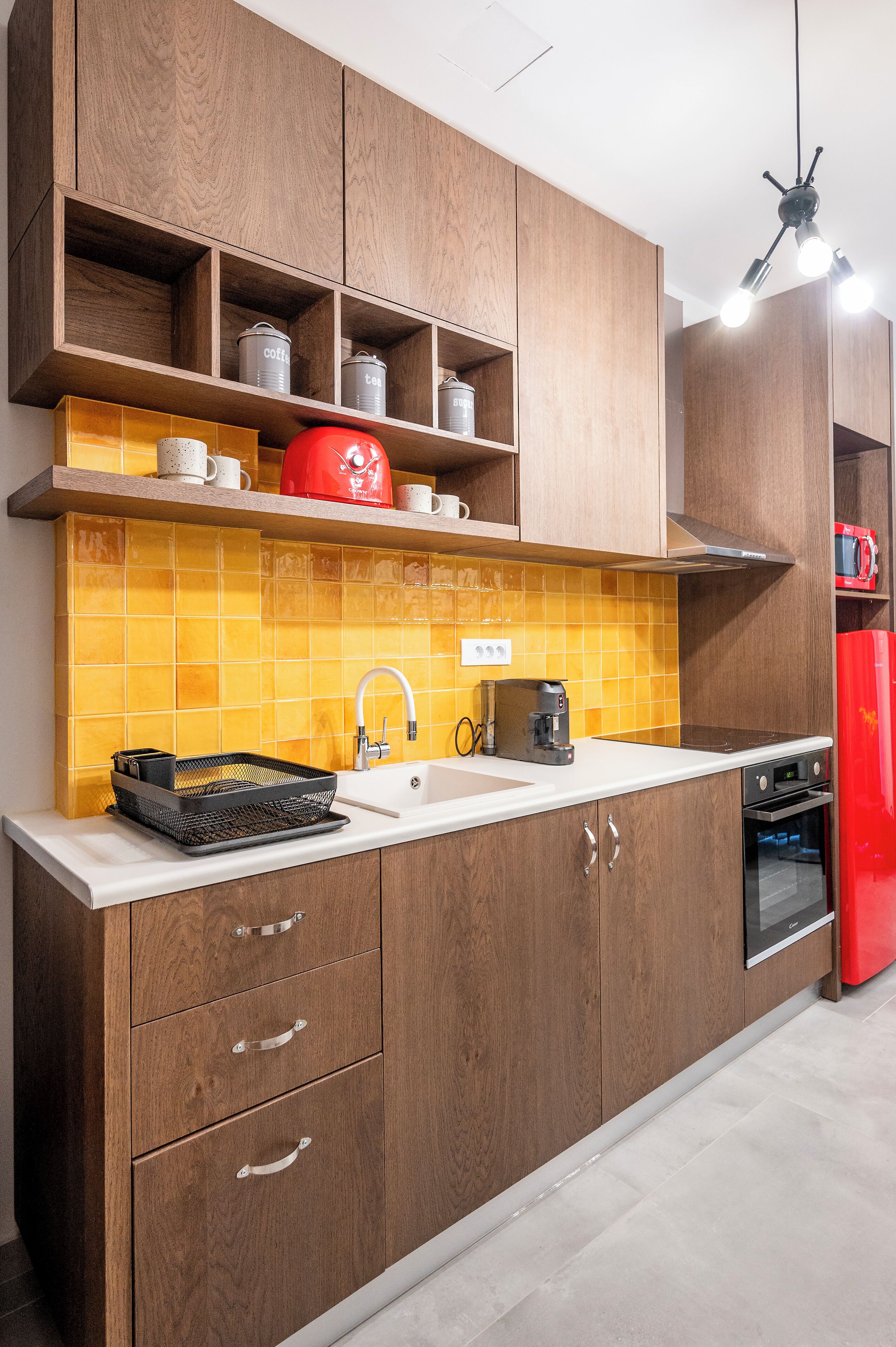 Une cuisine avec des meubles de rangement en bois, un crédence jaune carrelée, une bouilloire rouge et un réfrigérateur rouge.