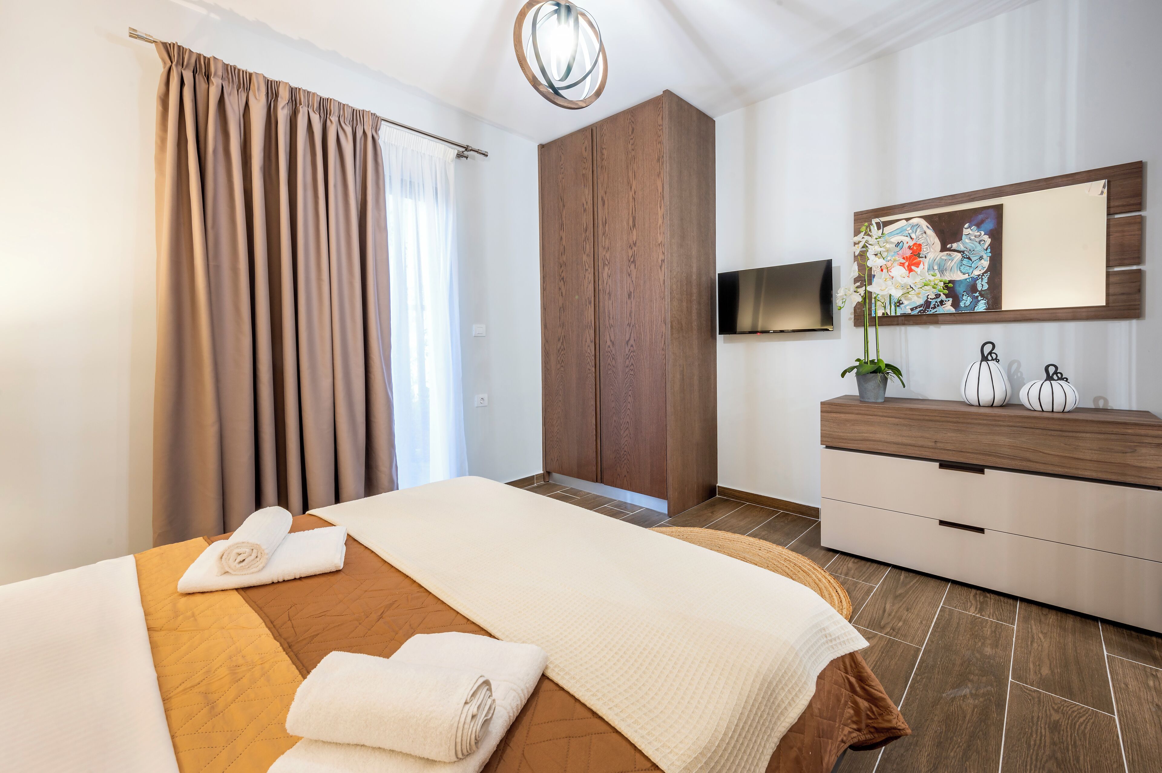 A hotel room with a bed, a wooden wardrobe, a flat-screen TV, and a decorative mirror.