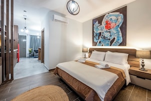 Una habitación de hotel moderna con una cama grande, una mesita de noche, un cuadro colgado en la pared y vistas a la habitación contigua.