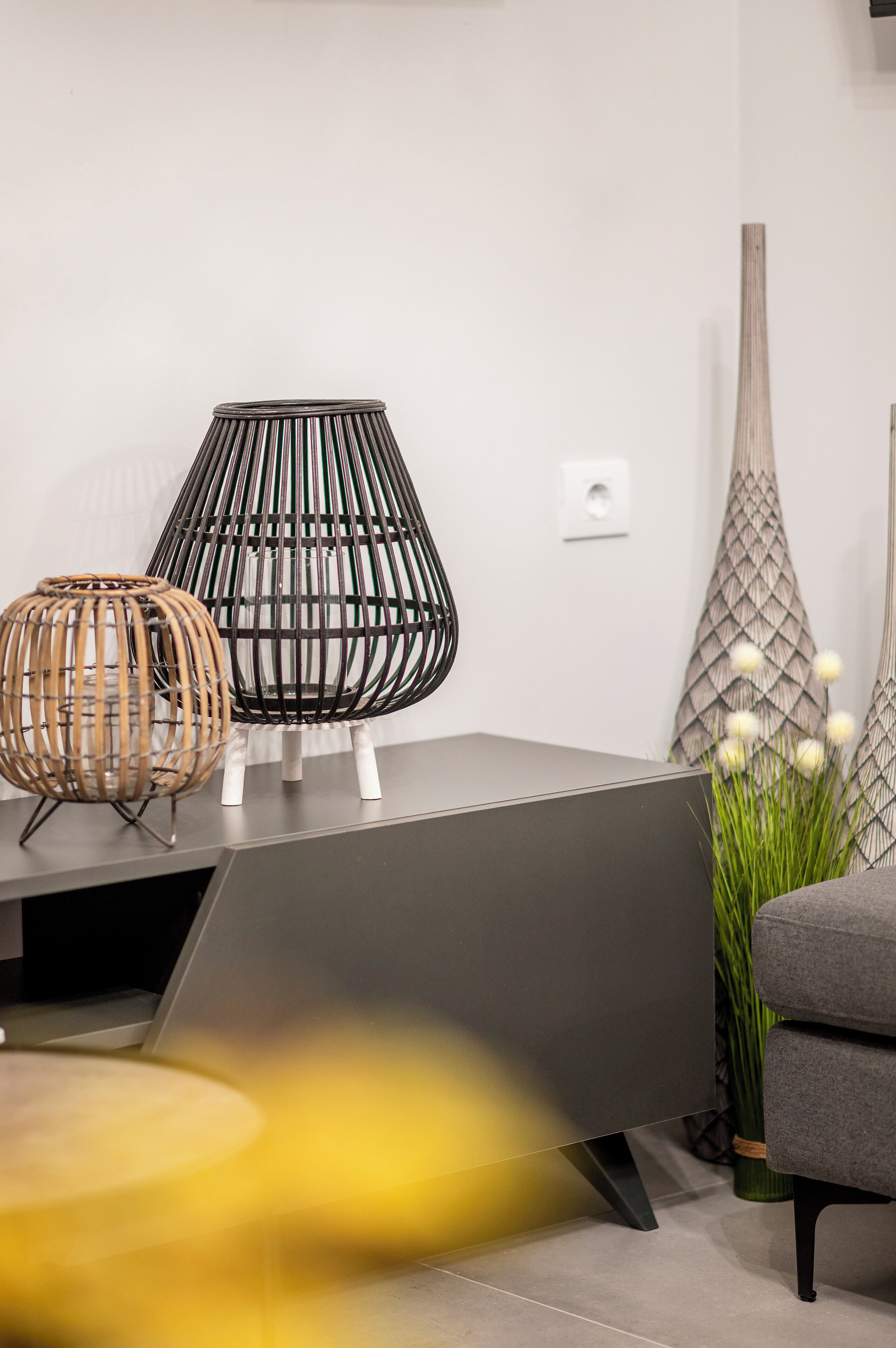 Een moderne woonkamer met een grijze bank, een zwart-wit lamp en een decoratieve vaas met witte bloemen.