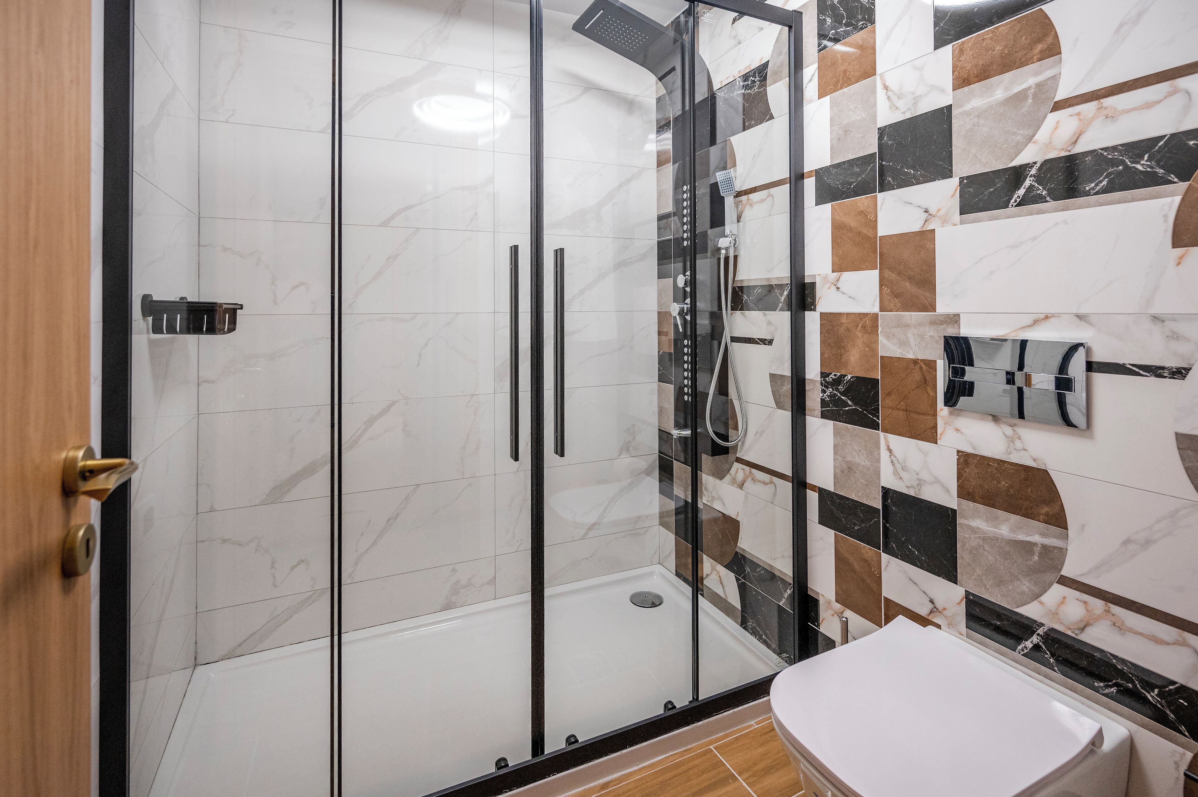 A modern bathroom with a glass-enclosed shower, a white toilet, and a tiled wall with a geometric pattern.