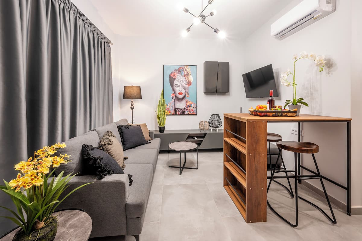 Een moderne woonkamer met een grijze bank, een klein rond tafeltje en een houten bar met krukken.