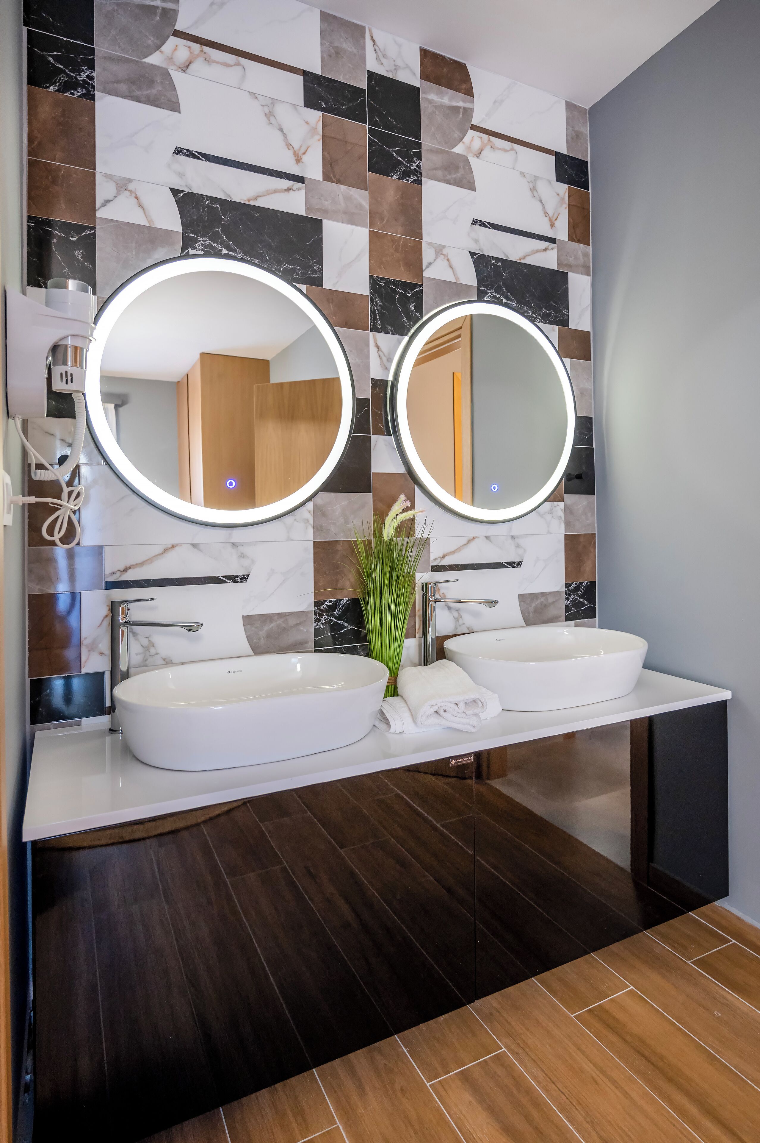 Un bagno moderno con due lavabi, uno specchio grande e un pannello decorativo in piastrelle.