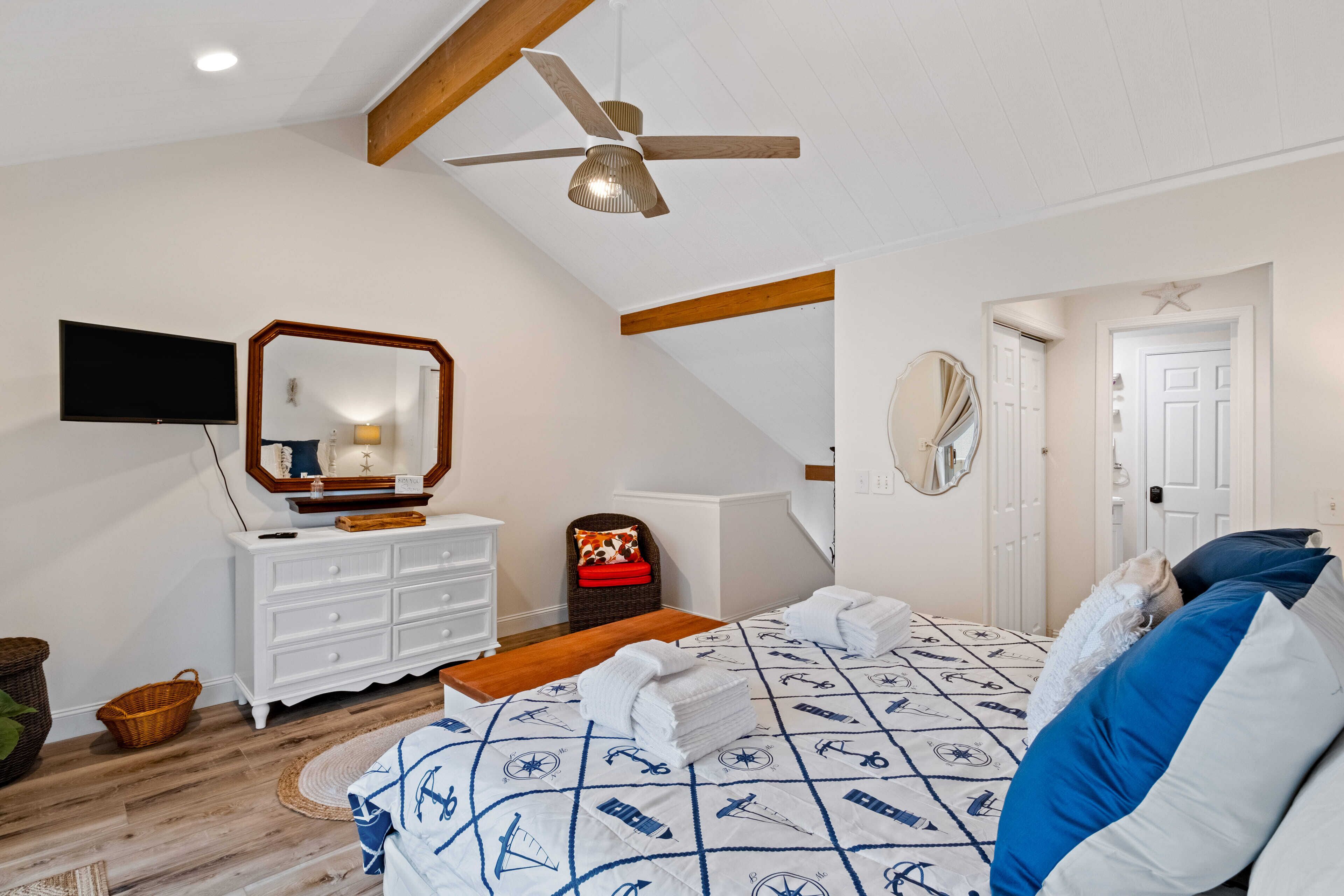 A bedroom with a bed, a dresser, a television, a ceiling fan, and a door.