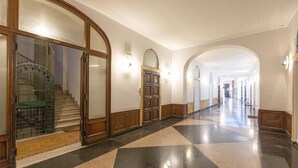A long, polished hallway with a checkered floor, wooden doors, and a staircase with a green railing. - Corso View apartment (Rome)