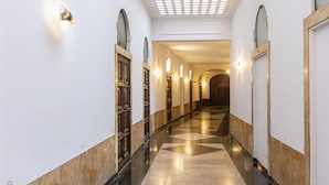 A hotel corridor with a checkered floor, arched doorways, and wall-mounted lighting. - Corso View apartment (Rome)