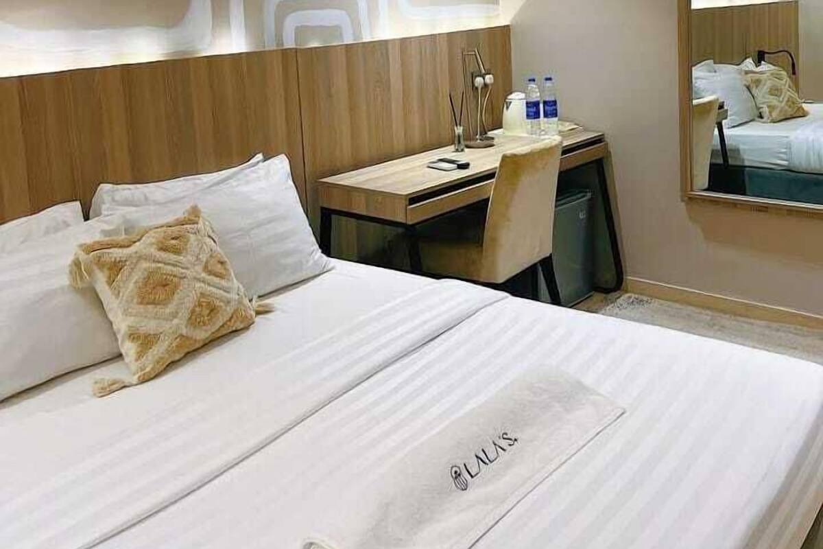 A hotel room with a bed, a desk, a chair, a mirror, and a wall with a geometric pattern.