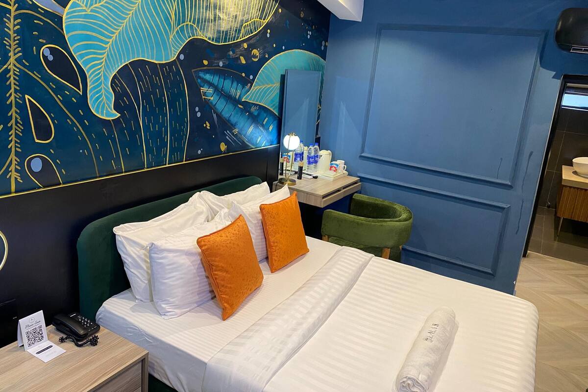 A hotel room with a bed, a desk, a chair, and a wall with a mural.