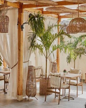 A cozy outdoor dining area with wicker furniture, hanging baskets, and a central potted plant. - LALA'S LAGOS LTD (Lagos)