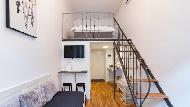 A room with a bed, a small desk, a TV, and a staircase. - Rhino Studios (Ljubljana)