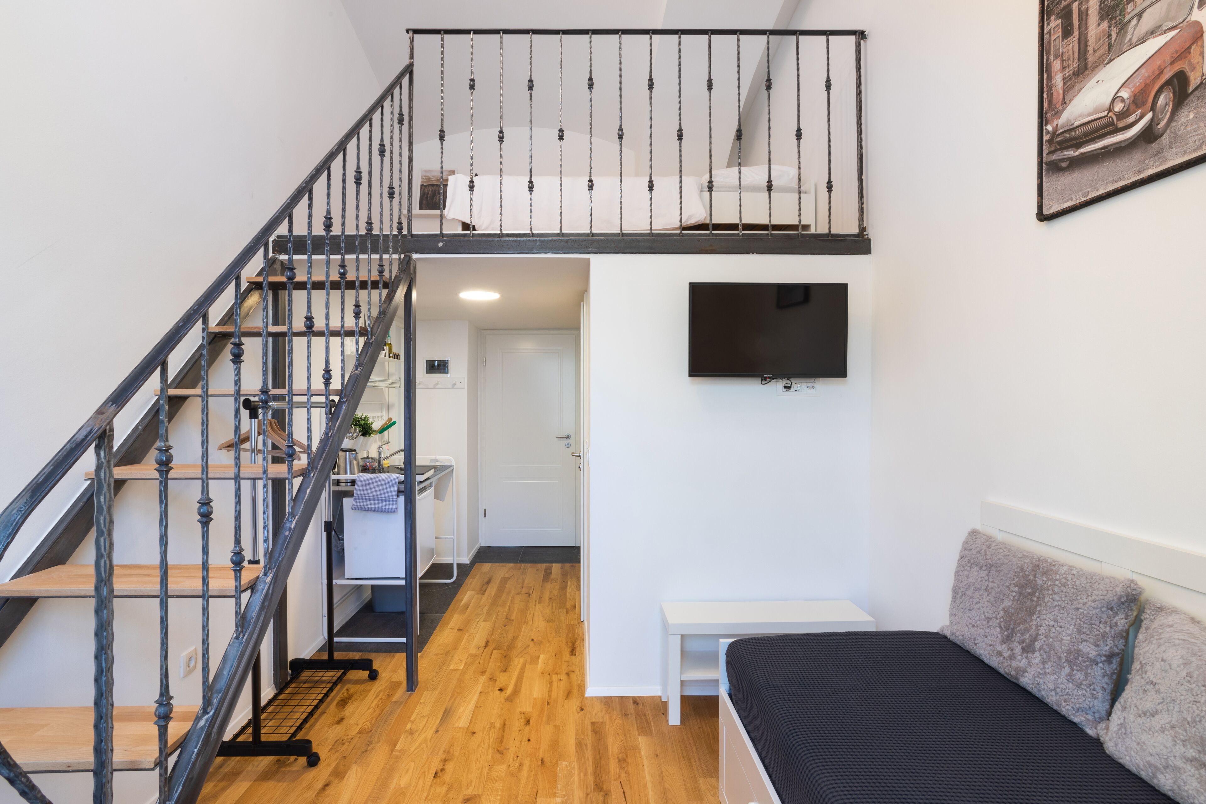 A bedroom with a bed, a TV mounted on the wall, a staircase, and a small desk area.