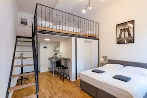 A compact room with a loft bed, a small kitchenette, and a staircase.