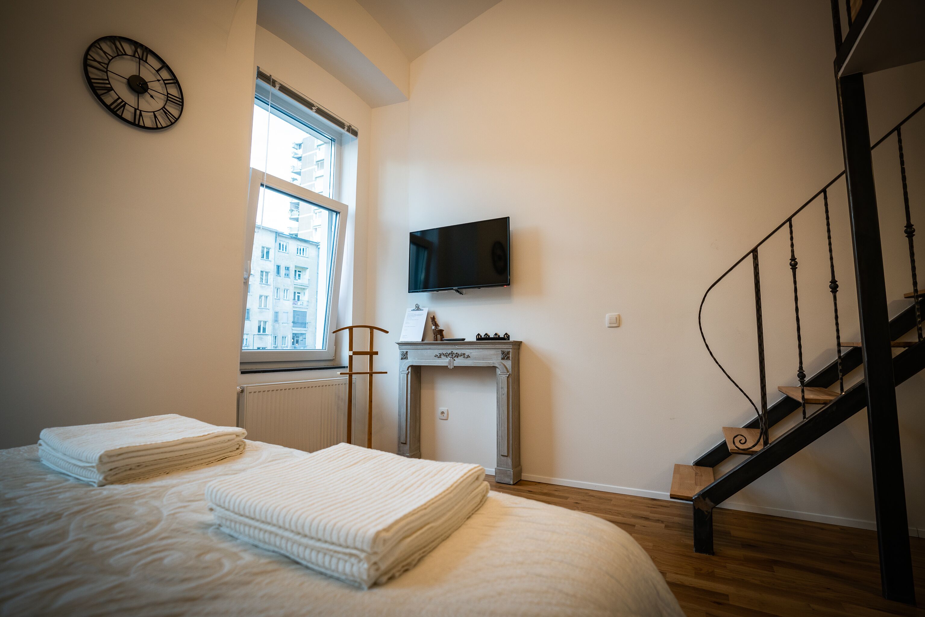 A bedroom with a bed, a TV mounted on the wall, a fireplace, and a staircase.