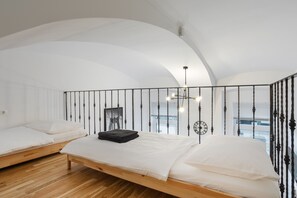 A bedroom with two beds, wooden flooring, white walls, a black railing, and a hanging light fixture. - Rhino Studios (Ljubljana)