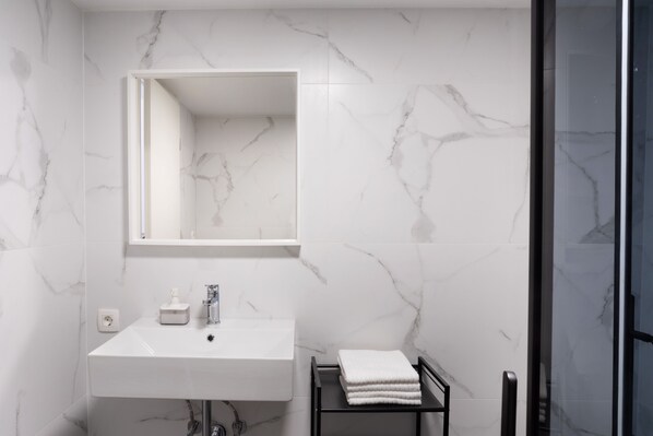 A modern bathroom with a white marble sink, a mirror, and a black towel rack.