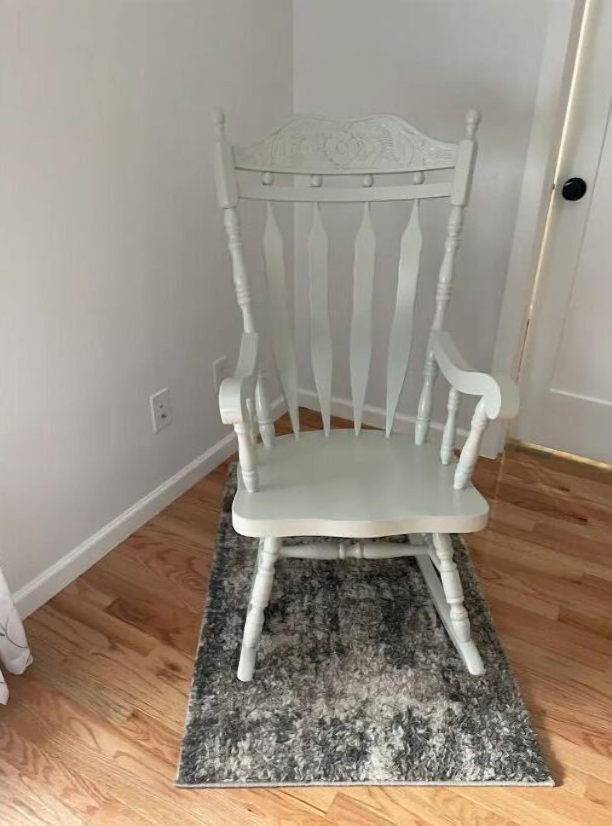 Une chaise en bois peinte en blanc, dotée d’un haut dossier et de pieds tournés, posée sur un tapis à motifs gris et noirs.