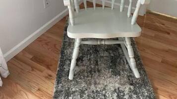 Une chaise en bois peinte en blanc, dotée d’un haut dossier et de pieds tournés, posée sur un tapis à motifs gris et noirs.