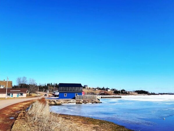 A waterfront property with a clear view of the water, a road, and a small building.