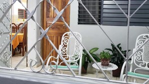 A balcony with white metal railings, a wooden door, and two white chairs with green cushions. - Hostal Bella Mar CIENFUEGOS (Cienfuegos)