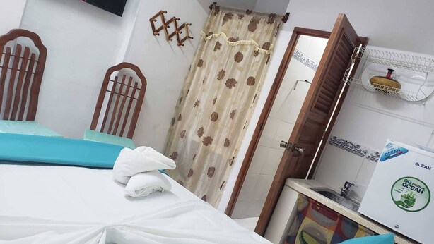 A bedroom with a bed, a TV mounted on the wall, a shower area, and a refrigerator with a green ocean-themed sticker. - Hostal Bella Mar CIENFUEGOS (Cienfuegos)