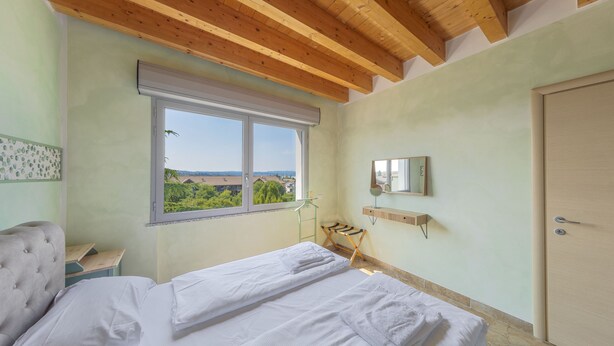 Ein Schlafzimmer mit Bett, einem Fenster mit Ausblick, einer Holzbalkendecke und einer Tür.