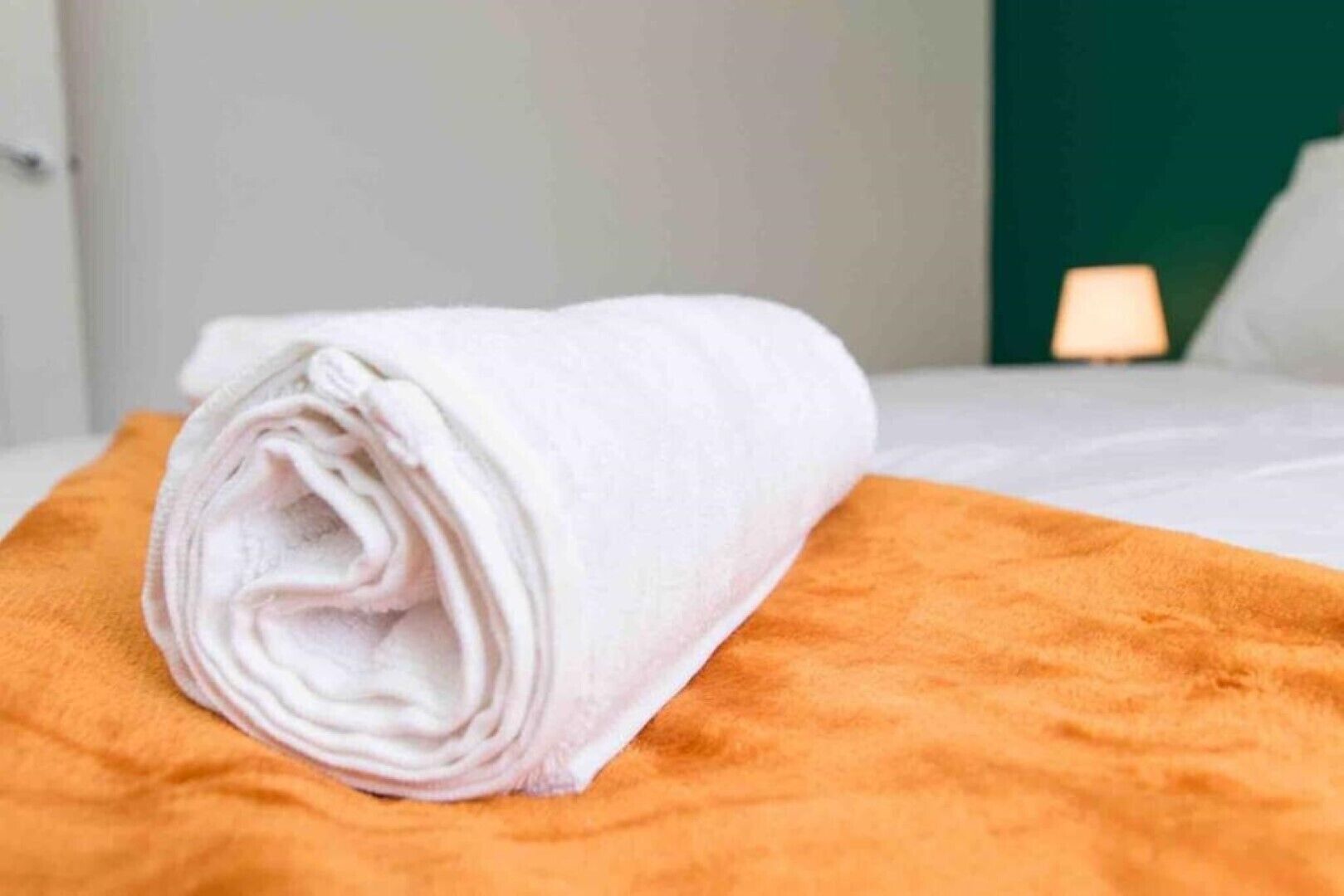 En prydligt vikt, vit handduk ligger på ett orangefärgat överkast i ett hotellrum.