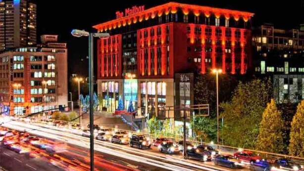 Un hotel ben illuminato con una facciata rossa evidente e il nome 'The Mailbox' ben visibile.