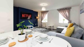Un soggiorno moderno con zona pranzo, un divano, un tavolino da caffè e una TV che mostra il logo di Netflix.