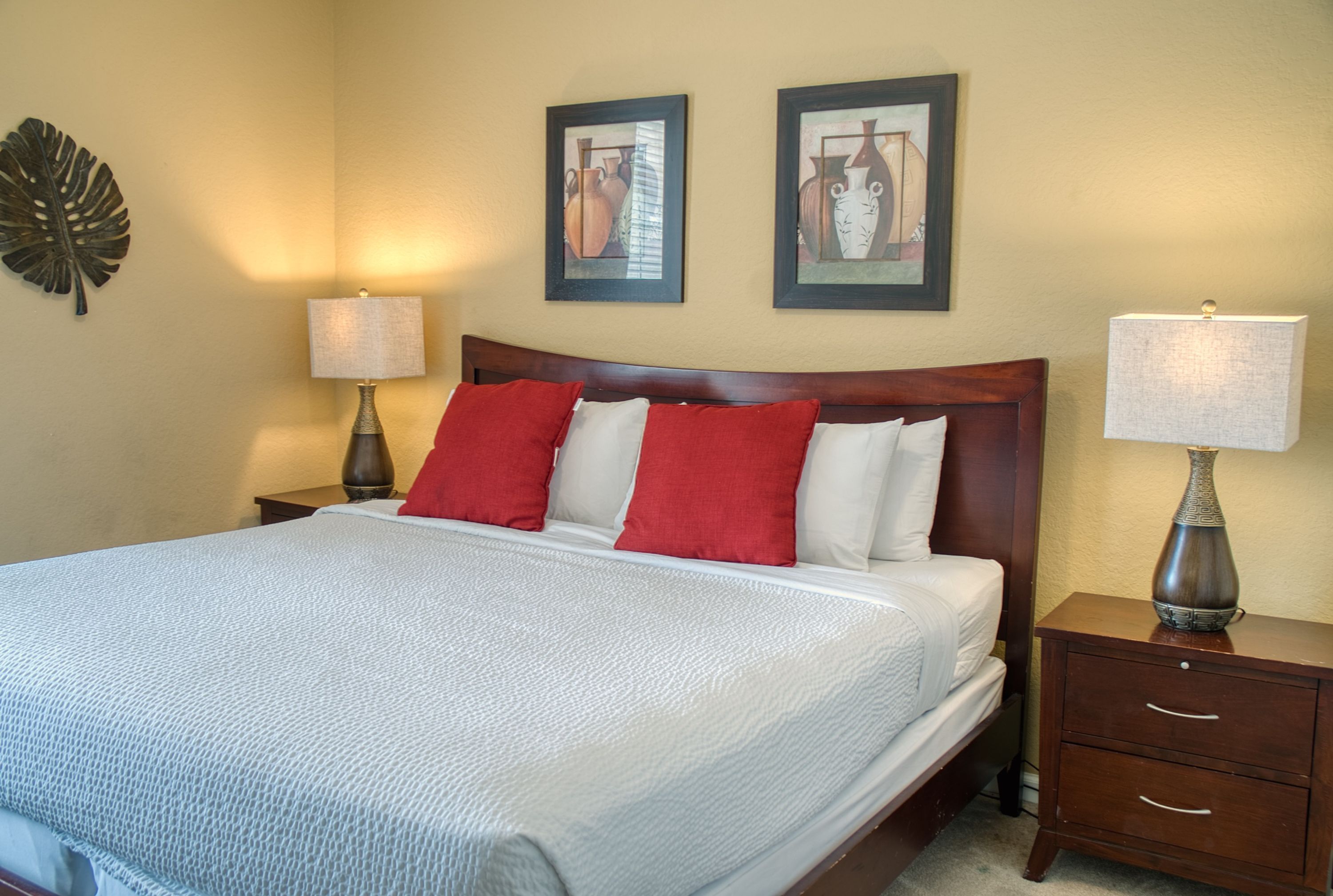 A neatly made bed with a white and red pillow arrangement, a wooden headboard, and two bedside tables with lamps.