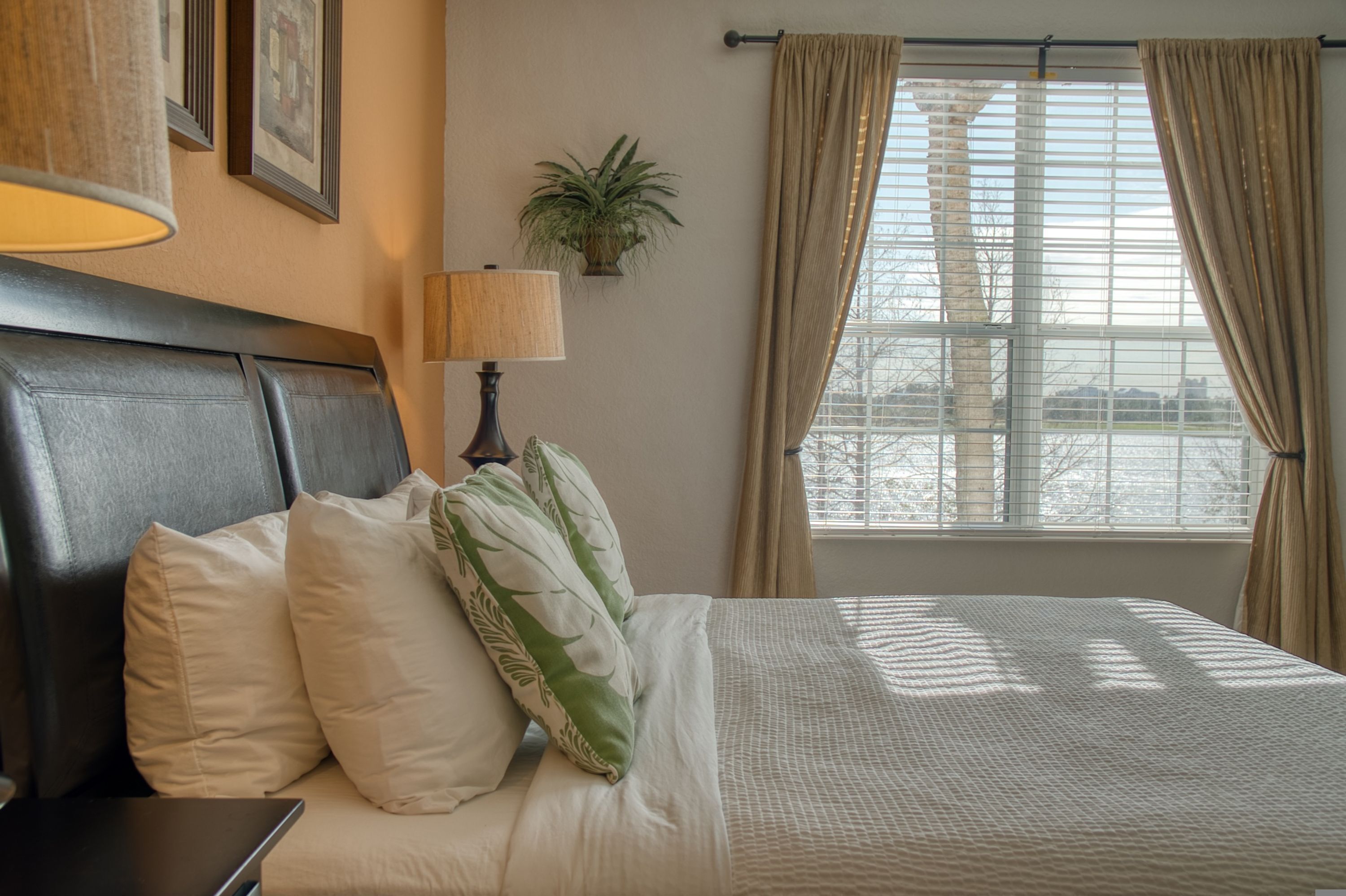 A neatly made bed with white and green pillows, a lamp, and a plant on the wall.