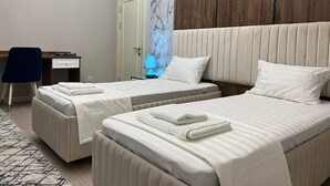 A hotel room with two beds, a desk, a chair, and a nightstand with a lamp. - Nur Makon (Tashkent)