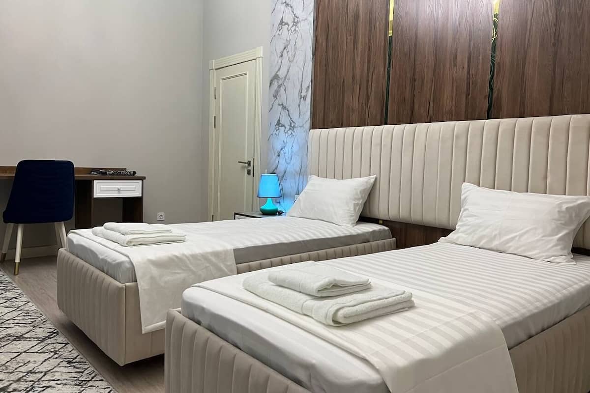 Habitación de hotel con dos camas, un escritorio, una silla y una mesita de noche con lámpara.
